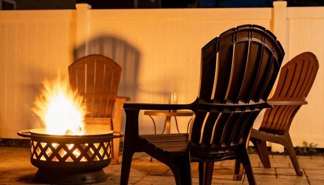 Adirondack chairs glowing by fire pit on backyard patio at night, warm cozy intimate ambiance