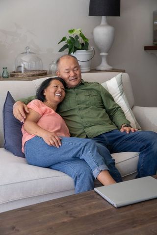 Chinese couple relaxing on couch, cuddling and smiling in cozy modern living room