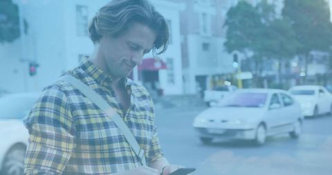 Young commuter in yellow plaid shirt standing at city corner checking phone, urban commute