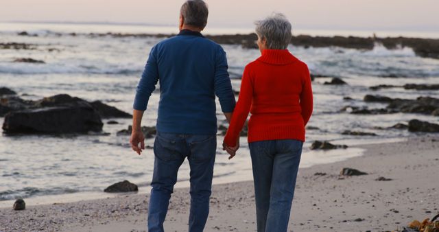 Senior caucasian couple holding hands and walking on beach by sea at sunset. Retirement, relationship, love, togetherness, free time and relaxing, unaltered.