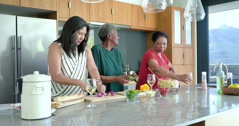 Multigenerational women preparing meal at modern kitchen island with wine and fresh produce
