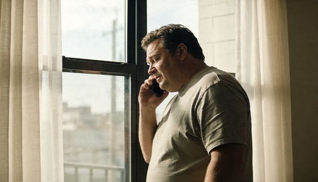 Midlife man talking on smartphone by sunlit apartment window, contemplative moment