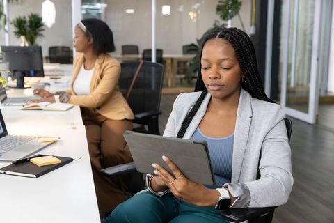 African american professional using tablet while colleague working at coworking desk