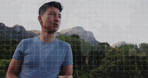 Asian man gazing over forested mountain viewpoint with rugged peaks and calm skyline