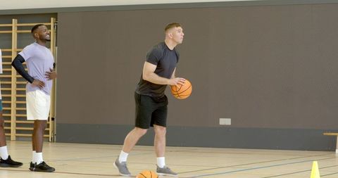 Athlete preparing to pass basketball during indoor passing drill with cone and teammates