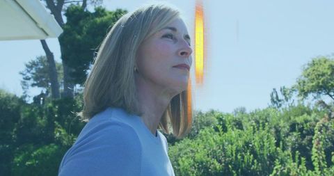 Mature woman gazing upward in sunlit garden with warm orange lens flare