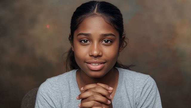South asian teen sitting clasping hands under chin closeup headshot with warm gaze