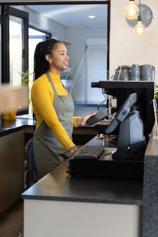 Smiling african american barista preparing espresso and holding portafilter at bright modern cafe