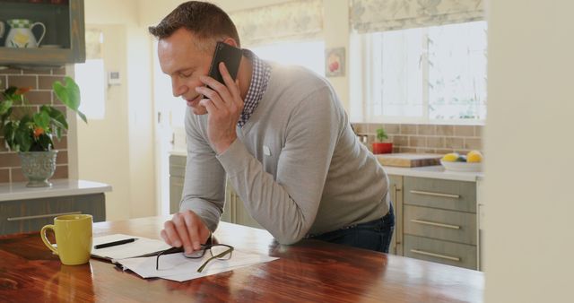 Smiling Man on Phone Handling Financial Documents in Kitchen - Download Free Stock Images Pikwizard.com