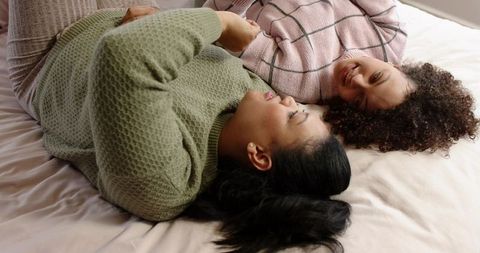 Lying head-to-head friends sharing cozy conversation in knit sweaters on bed