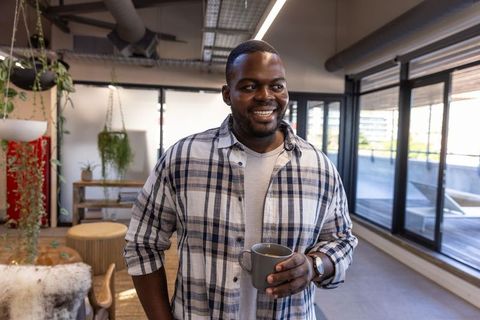 Smiling african american man relaxing with mug in modern coworking space