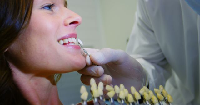 This image shows a dentist comparing tooth shades with a female patient's teeth, highlighting dental care services and procedures. Ideal for use in dental clinic websites, oral health campaigns, or educational materials on dental hygiene and treatments.