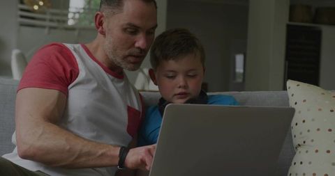 Father and son learning together on sofa using laptop for homework, teaching and bonding
