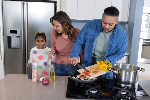Multicultural family cooking at kitchen island, dad adding sliced vegetables to pan