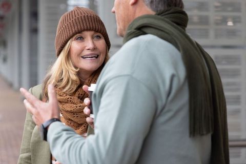 Middle-aged couple chatting outdoors over coffee in cool weather with beanie and knit scarf