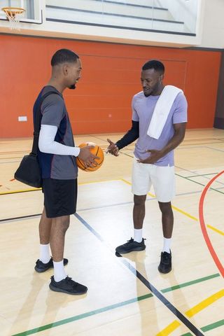 Two teammates discussing basketball strategy on indoor gym court during training session