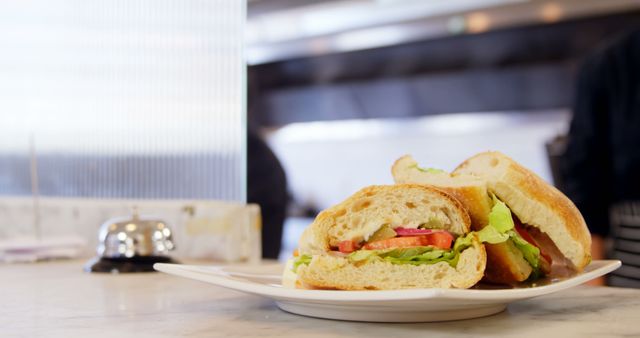 A freshly made sandwich with lettuce and tomato sits on a plate in a kitchen setting, with copy space. Its presentation suggests a casual dining experience or a quick meal option in a café or diner.
