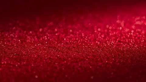Shimmering red glitter surface catching light with bokeh sparkle and metallic texture