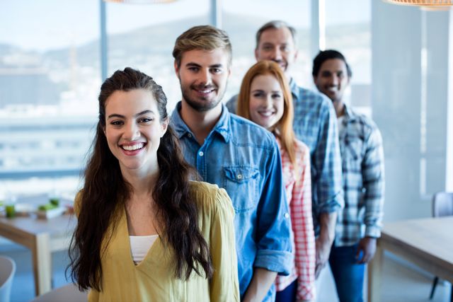 Group of diverse colleagues standing in a line in a modern office, smiling and looking at the camera. Ideal for use in articles or advertisements about teamwork, corporate culture, modern workplaces, and professional collaboration.