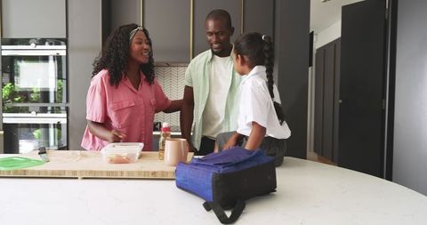 Black parents chatting with daughter sitting on kitchen island with school backpack
