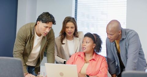 Multiracial team collaborating around laptop in modern office meeting