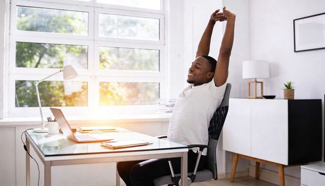 Relaxed remote worker stretching at sunlit minimalist home office desk, productivity break