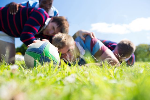 Close up of men playing rugby while lying at grassy field on sunny day