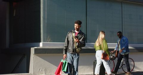Young adults walking sidewalk with shopping bags, pulling suitcase, carrying bike helmet