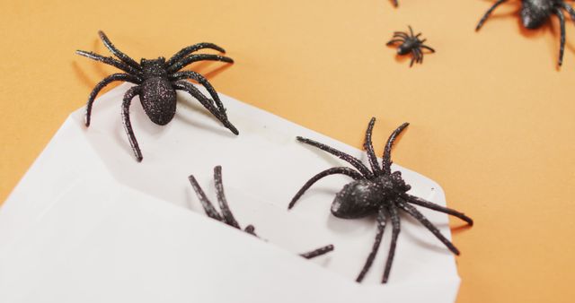 Multiple spider toys coming out of a envelope against orange background. halloween festivity and celebration concept