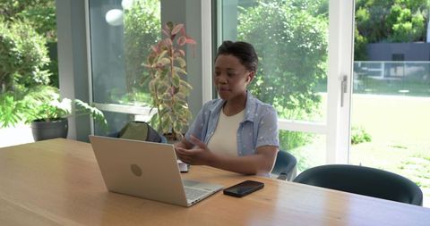 African woman working remotely on laptop in bright home workspace with smartphone