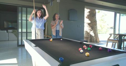 Joyful women cheering pool shot in sunlit modern home lounge