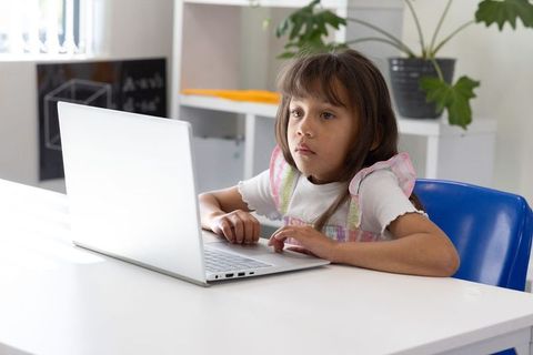 Young girl using laptop at bright home study desk for online learning and focus