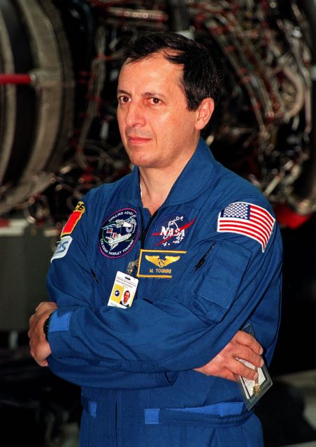 French astronaut Michel Tognini stands in NASA's Space Shuttle Main Engine Facility, wearing his blue space suit with badges and a flag. Ideal for articles about space missions, astronaut training, NASA projects, and international cooperation in space programs.