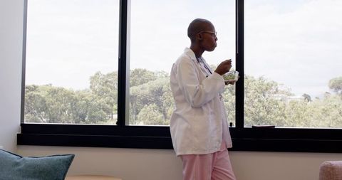 African american clinician enjoying lunch at window in scrubs and lab coat