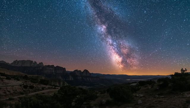 Milky way rising and arching over desert canyon with silhouetted mesas at night