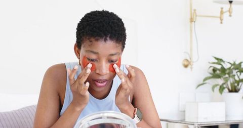 African american woman 20s applying red under-eye patches at vanity for glowing skin