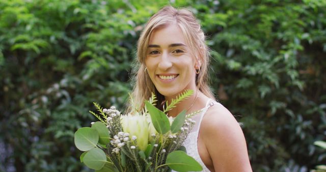 Portrait of happy caucasian woman holding bunch of flowers in garden on sunny day. wedding day and celebration concept.