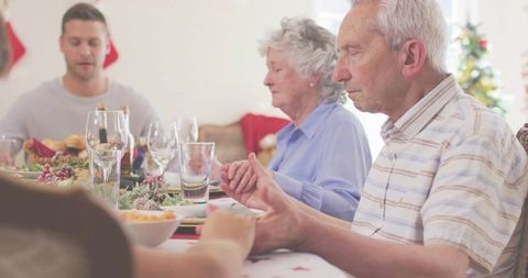 Multigenerational Family Holding Hands in Prayer at Festive Holiday Dinner Table Together