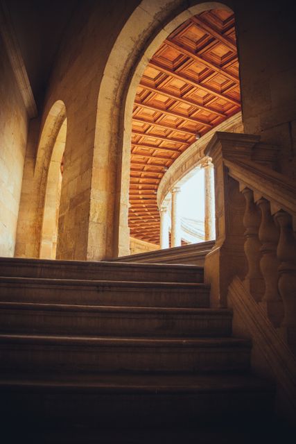 This image depicts a stone staircase leading towards a sunlit archway, with classical columns lining the sides and a wooden ceiling overhead. The architectural elements suggest historic significance and ancient design. This image can be used for projects related to architecture, history, cultural heritage, interior design, and educational materials on classical architecture.