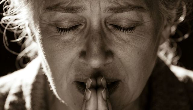 Senior woman praying with folded hands closeup monochrome emotional portrait