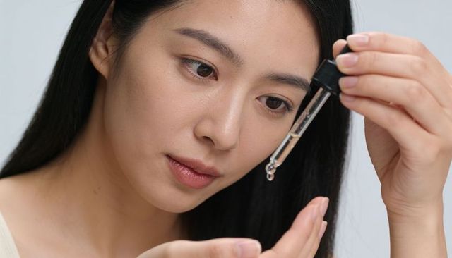 Asian woman applying facial serum with glass dropper for hydrated glowing skin