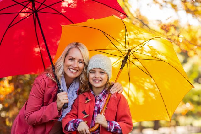 Portrait of cheerful girl holding umbrella with mother at park