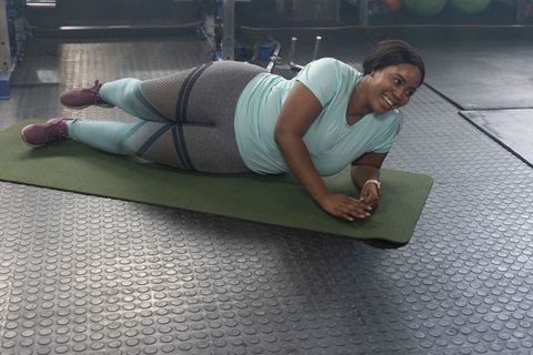 African american plus size woman performing side plank smiling on mat in gym strength training