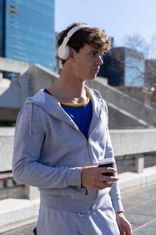 Young man wearing headphones holding coffee on urban bridge morning commute
