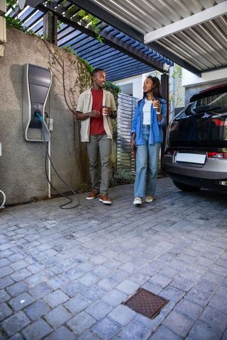 African American Couple Walking Near EV Charging Station with Coffee