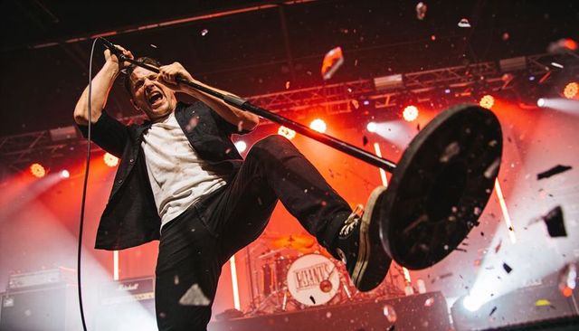Screaming rock vocalist kicking mic stand during high-energy live concert performance
