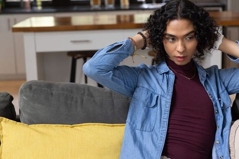 Non-binary person reclining on gray couch adjusting hair in modern home interior