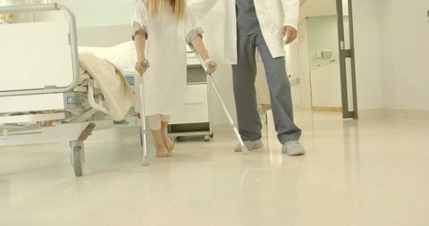 Child walking with forearm crutches while doctor assisting in pediatric hospital corridor