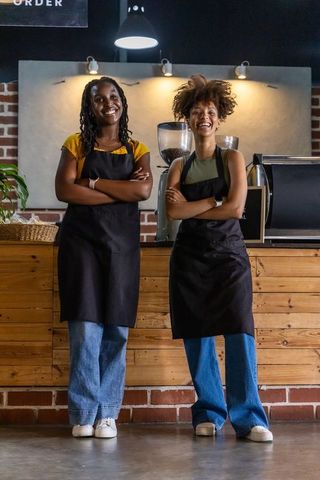 Smiling baristas standing behind wooden counter wearing black aprons in coffeehouse