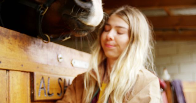 Young woman interacting with horse in a stable, showcasing the bond between humans and animals. This image captures the essence of rural life and equestrian activities. It can be used in articles about animal care, farm lifestyles, human-animal relationships, veterinary services, or equestrian sports.